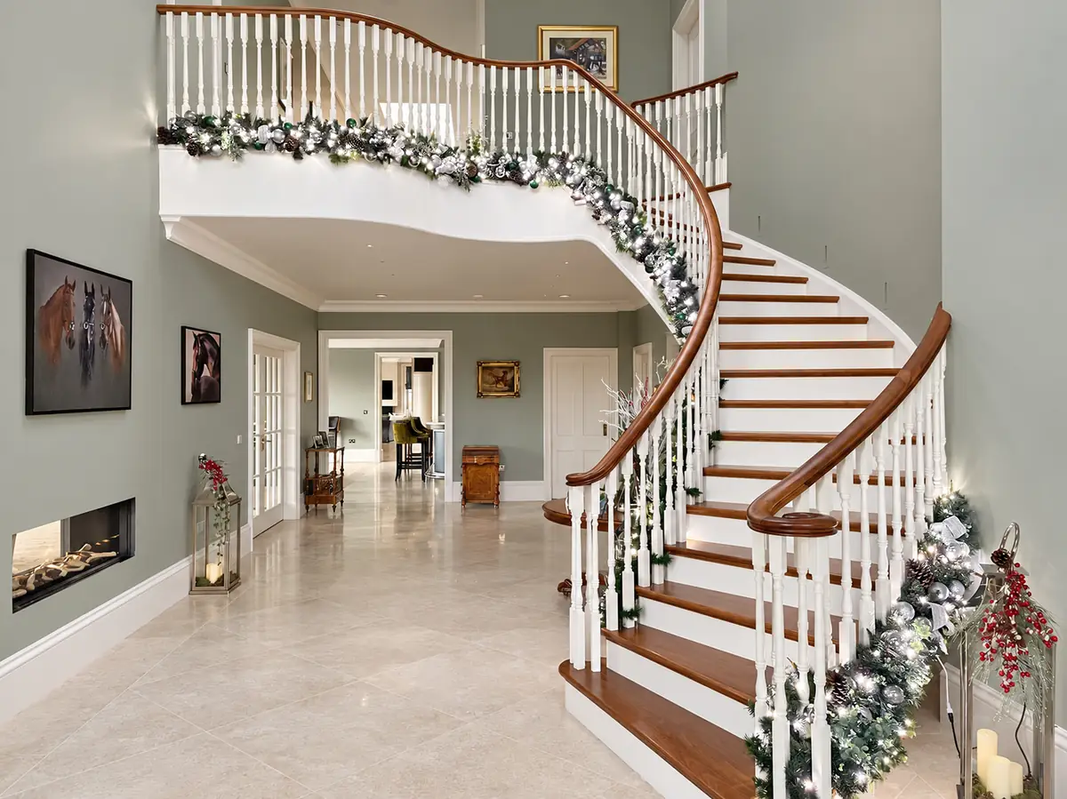 Sweeping staircase in an entrance hall dressed with a lit silver and green garland