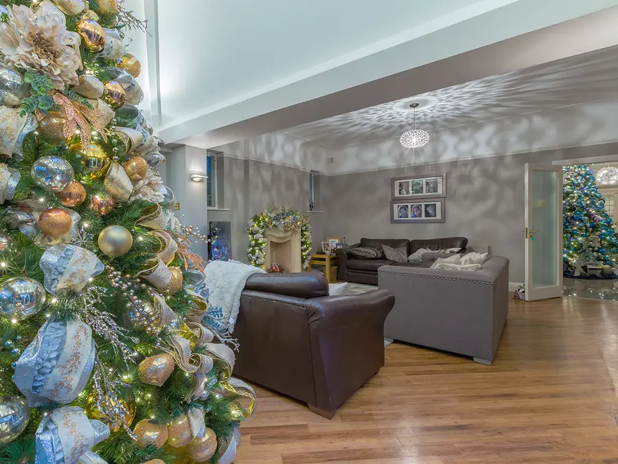 Open-plan living room with a silver and gold ribboned Christmas tree, a garlanded fireplace and a second tree through the doorway