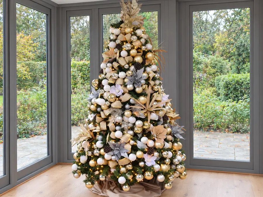 Christmas tree in a garden room decorated with gold, silver and white baubles and ribbon